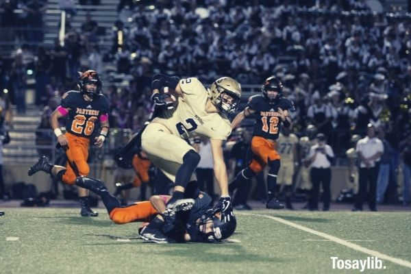 football player in white tackling another player in black on football field people watching