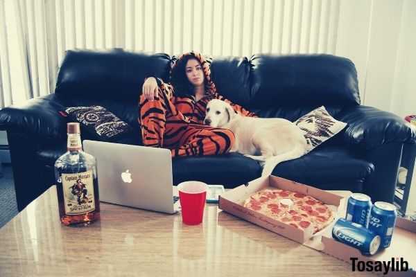 woman on the black sofa wearing tiger costume beside the white dog with laptop bear pizza in front