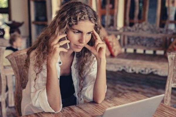 photo-of-blonde-curly-haired-woman-trying-to-find-excuses-to-get-off-the-phone-quickly-while-in-front-of-laptop