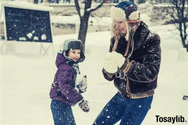 woman and child wearing snow attire playing with snow