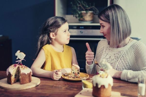 how to say yes young girl in yelow mom in white knitted tops thumbs up to her child eating cake
