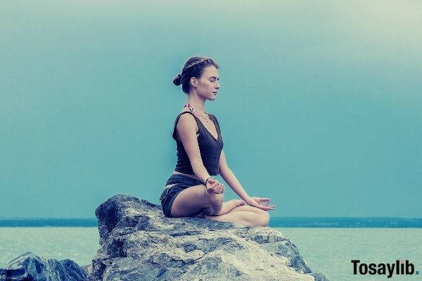 concentrated yoga teacher wearing tank top meditating on large stone skies sea