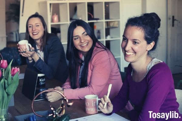 three women sitting by the table laughing while drinking on the mug