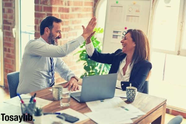 man and woman coworker happy high five office working formal attire laptop wooden table