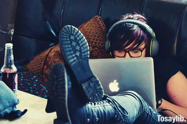 woman with red hair sitting on the chair feet on the table using macbook and listening to music