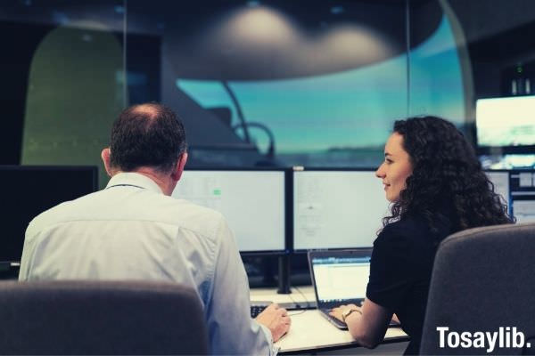 coworker woman in black shirt with curly hair laptop sitting beside old man wearing white long sleeves