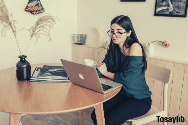 thoughtful female freelancer watching laptop in light room at home while having coffee