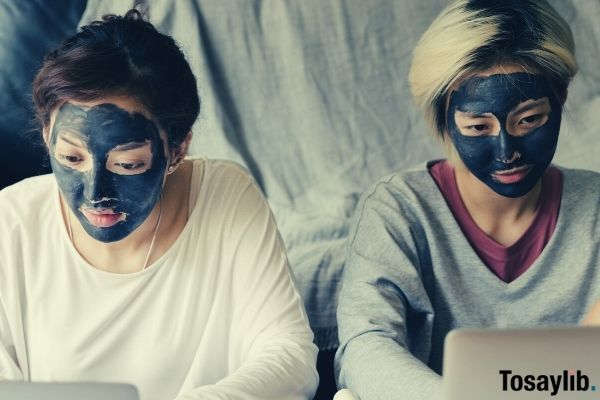 two women wearing longsleeves black facial masks while using laptops at home