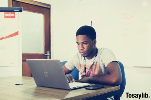 man in white shirt sitting in blue chair in front of table using HP laptop