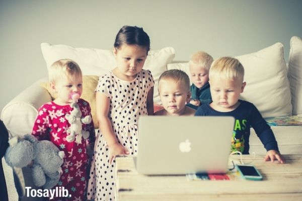 kids boys and girls cute watching something on the macbook near the sofa