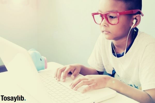 little boy listening and using laptop computer typing wearing white shirt and red glasses