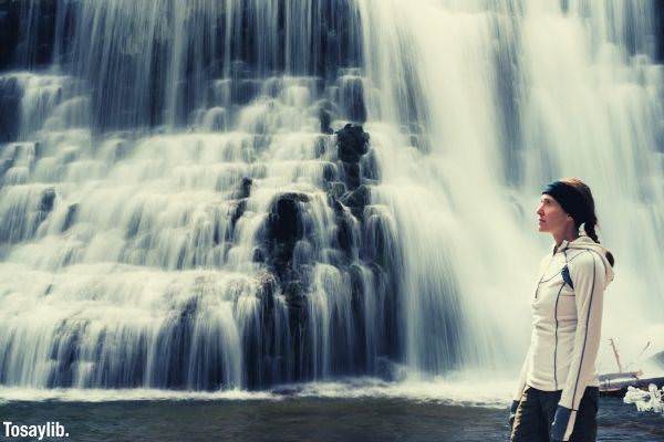 woman in white jacket long hair standing in front of waterfalls