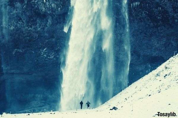 two people walking on ice time lapse photo of flowing waterfall