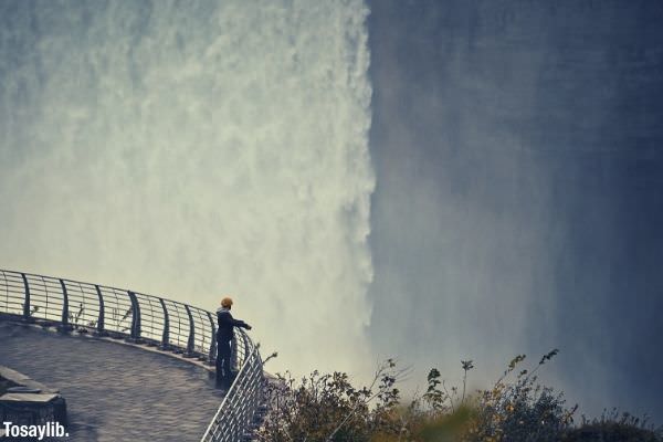 man standing fence concrete floor near edge beside waterfall