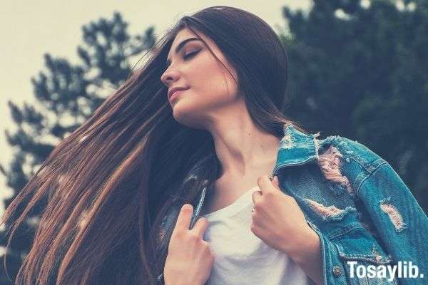 woman holding her blue jeans jacket and white shirt flipping her hair