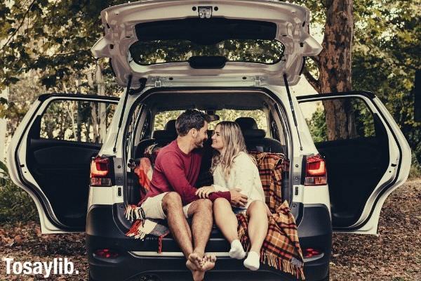photo of couple sitting in the back of car under a tree
