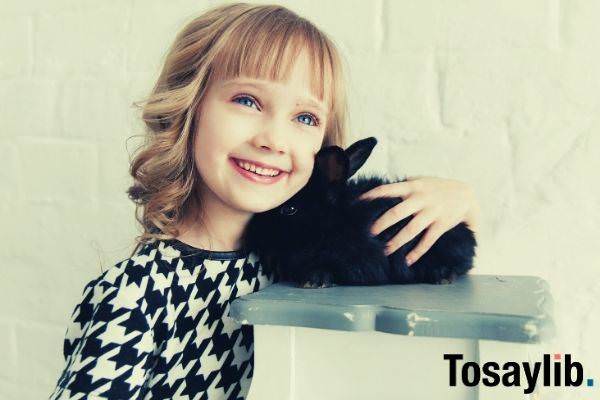 cute girl with blue eyes holding a black rabbit on top of gray wood surface