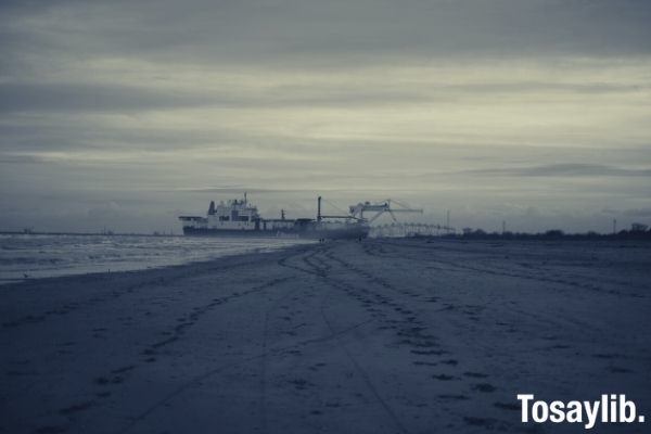 grayscale photo of beach with ship on the sea gray skies