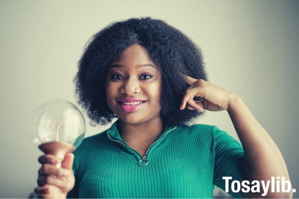 positive young african american lady holding light bulb in hand on gray background