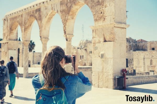 woman wearing jacket taking pictures of ruins using her camera