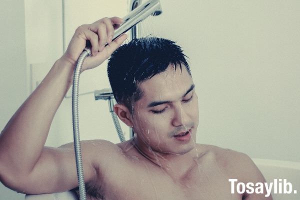 topless man in bathtub holding shower