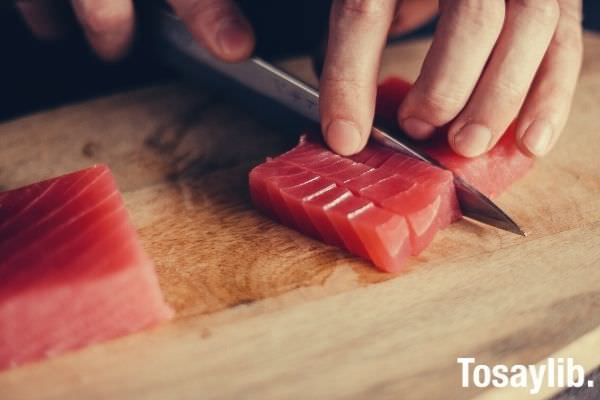 person slicing a fish for sushi on top of wooden chopping board