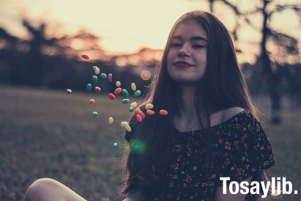 woman in black floral top playing with candies while sitting on the grass