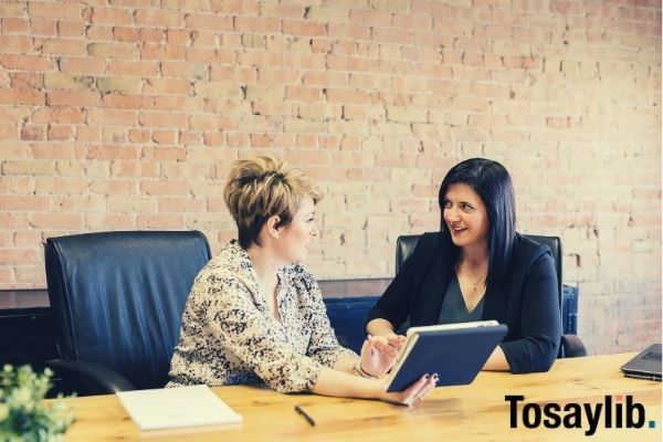 two women talking sitting on leather chairs in front of wooden table