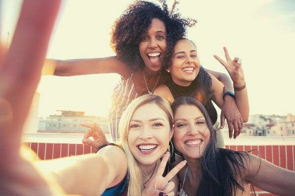 cheerful-young-diverse-women-showing-peace-sign-while-taking-selfie-on-rooftop-words-to-describe-laughter