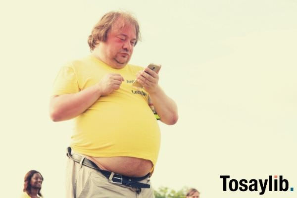 man in yellow shirt and brown pants using smartphone