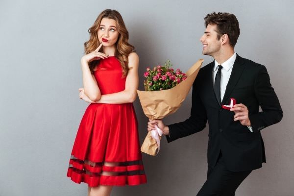 man wearing a suit giving a bouquet of flower to a girl thinking wearing red