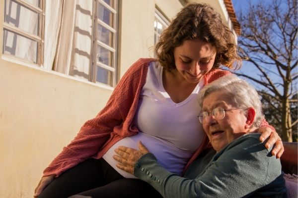 pregnant woman sits next elderly outside touching her tummy