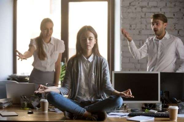 04 calm serene employee meditating office ignoring two colleagues