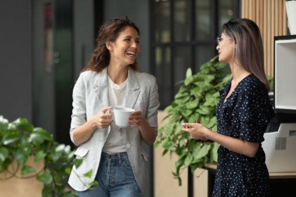happy positive female colleagues joking laughing holding a cup