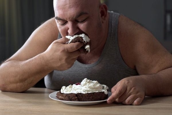 messy obese man greedily eating cake