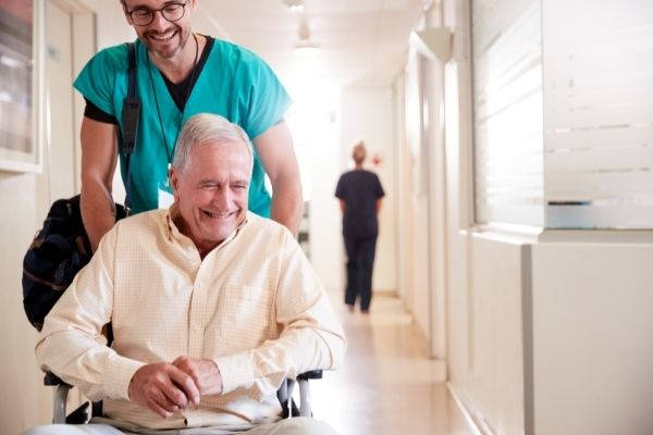 male wearing scrub suit pushing senior patient on a wheelchair