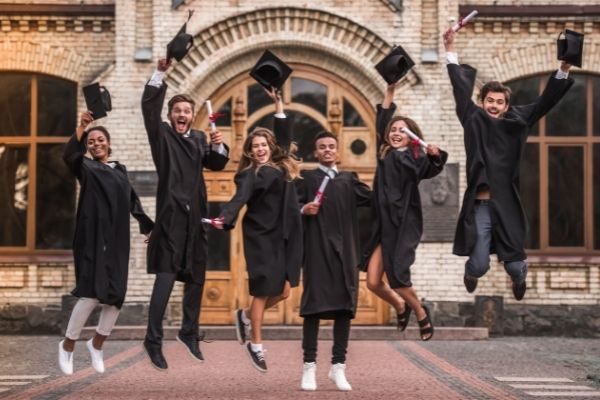 01 successful graduates academic dresses holding diplomas jump shot