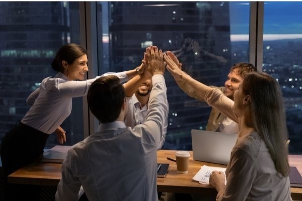 motivated multinational team raise high fives building window night