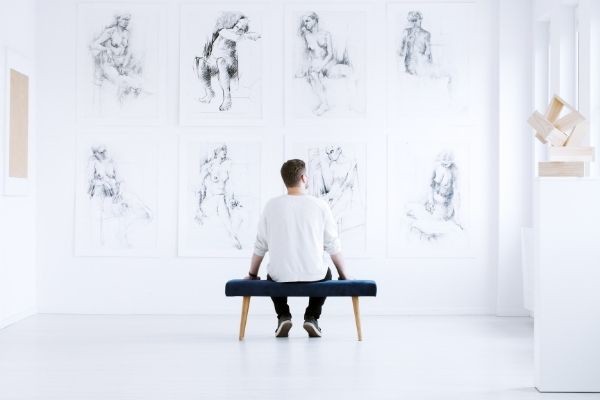 man relaxing art gallery while sitting looking on artworks