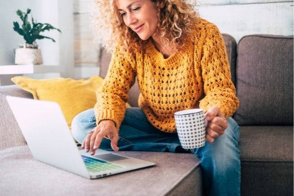 nice beautiful lady blonde curly hair typing on laptop holding mug