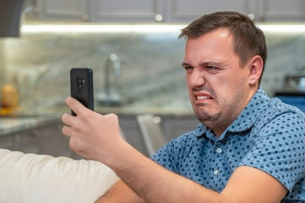 annoyed millennial man wearing polka dots disgust look smartphone