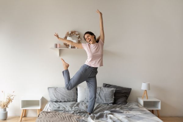 overjoyed funny woman jumping on comfortable bed