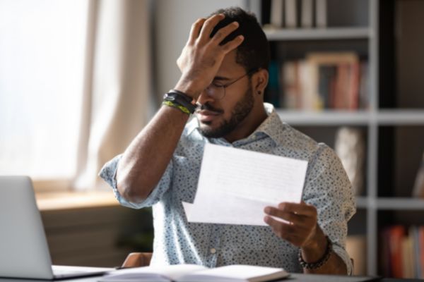 stressed african businessman sit desk holding his head while looking at the paper