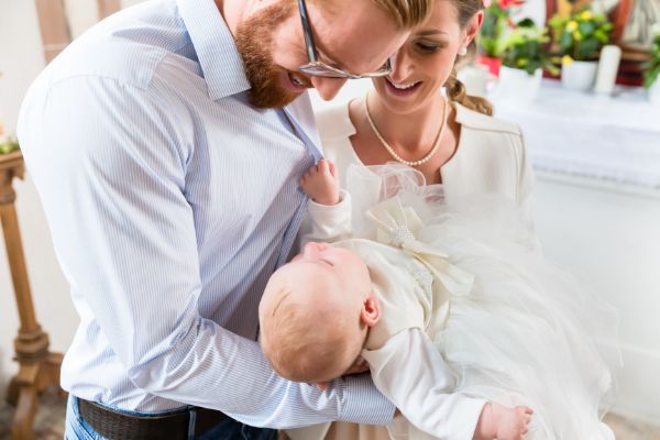 young parents church their baby wearing beautriful white baby dress
