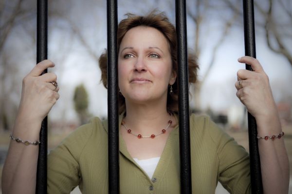 woman holding on jail bars looking outside sun