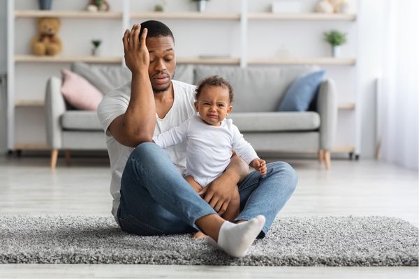 exhausted black young father sitting crying baby