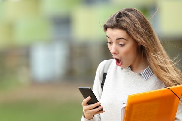astonished student receiving surprising news on smartphone