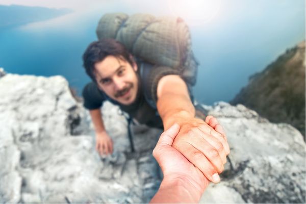 adventurers helping each other climb mountain