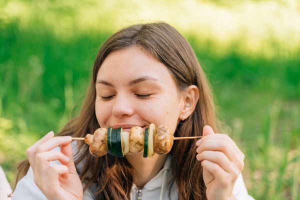 teenager girl eating grilled vegetables outdoors