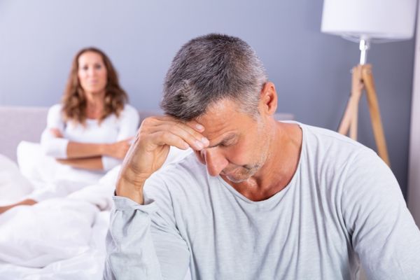 close depressed man sitting on bed touching head